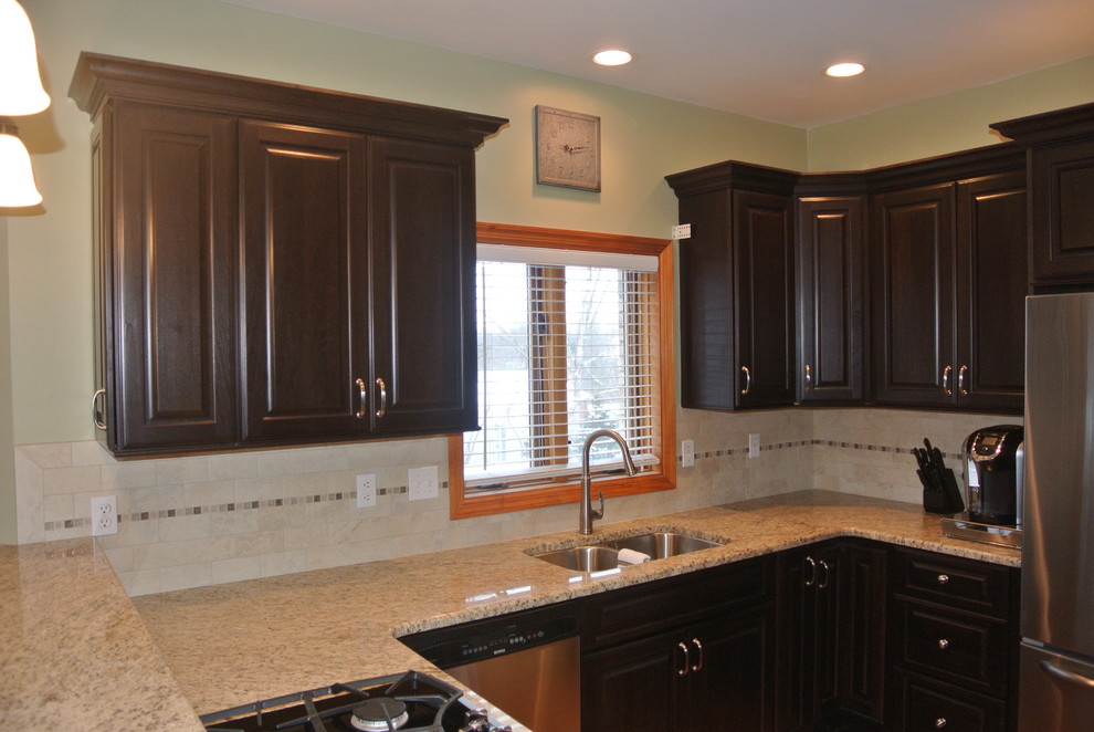 Inspiration for a mid-sized u-shaped medium tone wood floor eat-in kitchen remodel with a double-bowl sink, dark wood cabinets, granite countertops, beige backsplash, stone tile backsplash and stainless steel appliances