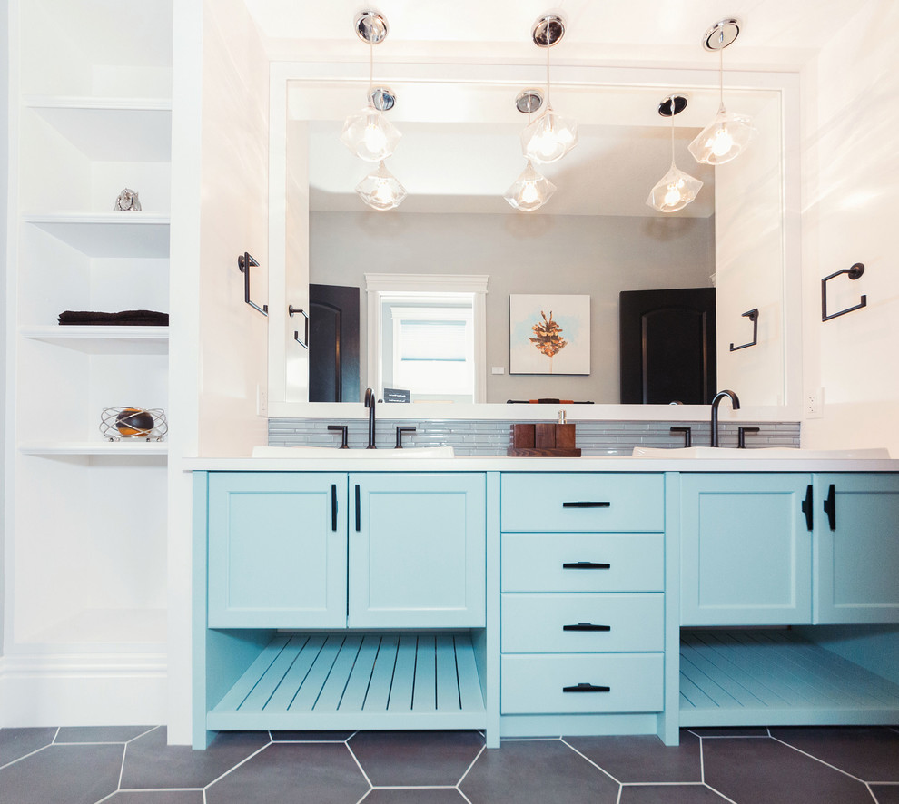 Photo of a mid-sized transitional kids bathroom in Edmonton with shaker cabinets, blue cabinets, an alcove tub, a shower/bathtub combo, a one-piece toilet, blue tile, glass tile, grey walls, ceramic floors, a drop-in sink and laminate benchtops.