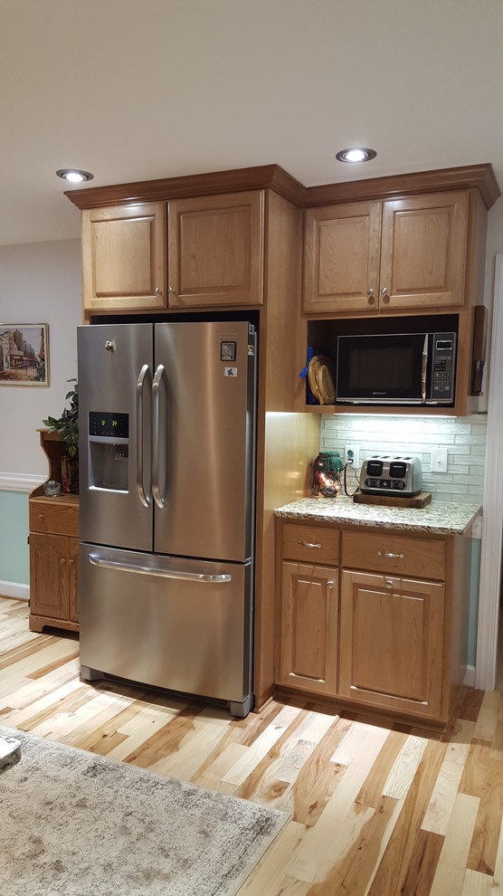 Small transitional u-shaped medium tone wood floor eat-in kitchen photo with an undermount sink, raised-panel cabinets, medium tone wood cabinets, granite countertops, glass tile backsplash, stainless steel appliances, no island and white backsplash