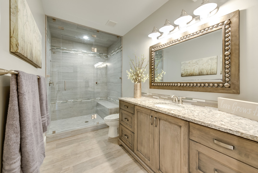 This is an example of a large transitional master bathroom in Salt Lake City with recessed-panel cabinets, an alcove shower, a two-piece toilet, beige tile, brown tile, gray tile, matchstick tile, grey walls, medium hardwood floors, an undermount sink, brown floor, medium wood cabinets, granite benchtops and a hinged shower door.
