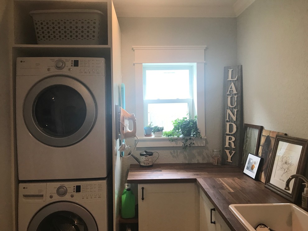 Design ideas for a small country l-shaped utility room in Tampa with a drop-in sink, shaker cabinets, white cabinets, wood benchtops, grey walls, brick floors, a stacked washer and dryer and beige floor.