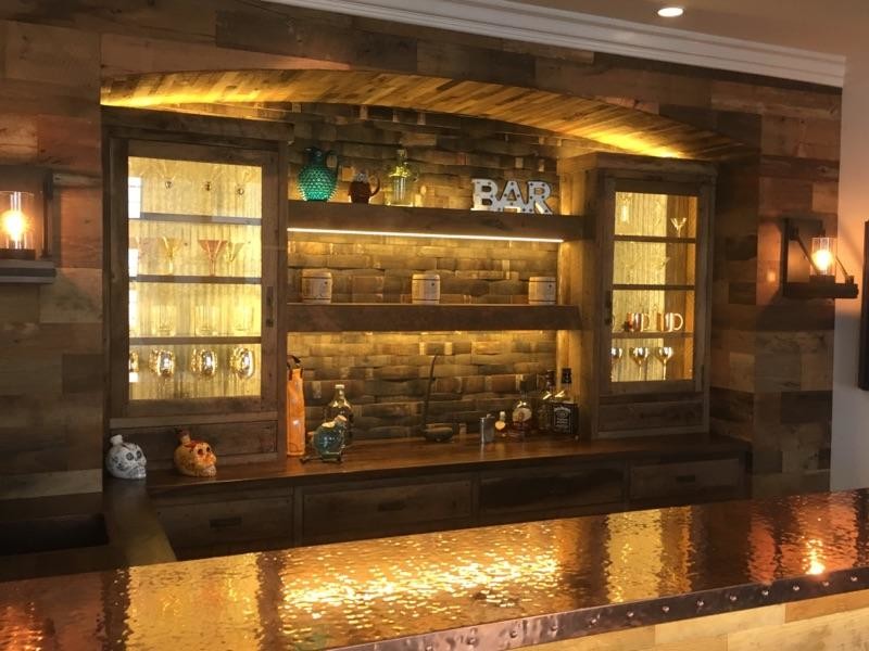 This is an example of a mid-sized country u-shaped wet bar in Orange County with a drop-in sink, shaker cabinets, medium wood cabinets, copper benchtops, brown splashback, timber splashback, dark hardwood floors and brown floor.