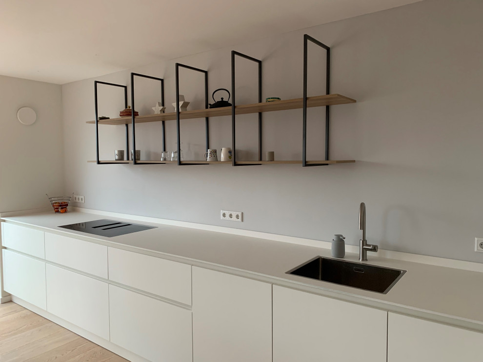 Diseño de cocinas en L moderna de tamaño medio abierta con armarios con paneles lisos, puertas de armario blancas, suelo de madera en tonos medios y encimeras blancas