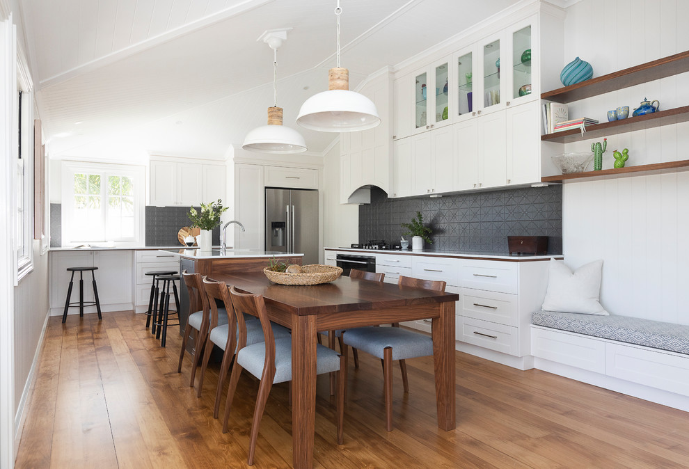 Photo of a traditional eat-in kitchen in Brisbane with a farmhouse sink, shaker cabinets, white cabinets, black splashback, medium hardwood floors and white benchtop.
