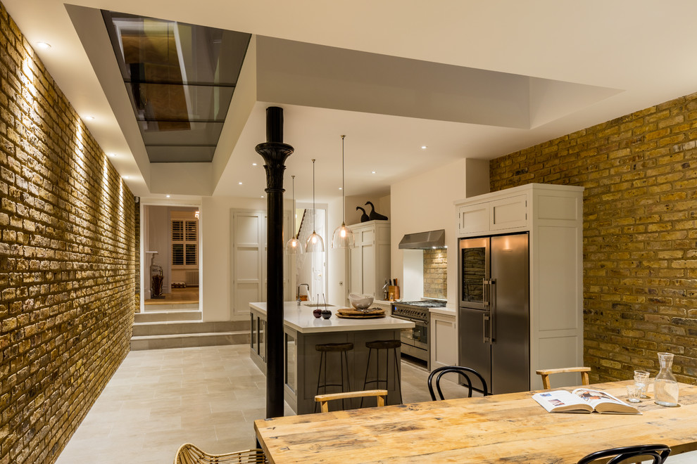 This is an example of a mid-sized traditional eat-in kitchen in London with an integrated sink, shaker cabinets, grey cabinets, solid surface benchtops, stainless steel appliances, limestone floors and with island.