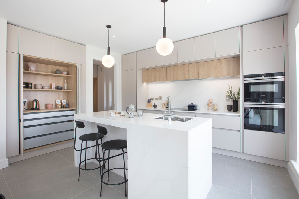 Contemporary l-shaped kitchen in Dublin with a double-bowl sink, flat-panel cabinets, white cabinets, white splashback, stainless steel appliances, with island, grey floor and white benchtop.