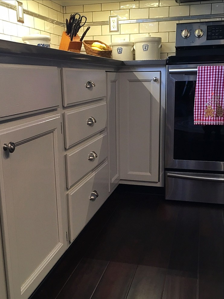 Example of a mid-sized transitional u-shaped medium tone wood floor enclosed kitchen design with an undermount sink, white cabinets, quartz countertops, white backsplash, subway tile backsplash, stainless steel appliances and an island