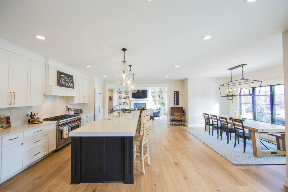 Large contemporary galley eat-in kitchen in Indianapolis with a farmhouse sink, recessed-panel cabinets, white cabinets, quartzite benchtops, white splashback, stone slab splashback, stainless steel appliances, medium hardwood floors, with island, brown floor and white benchtop.