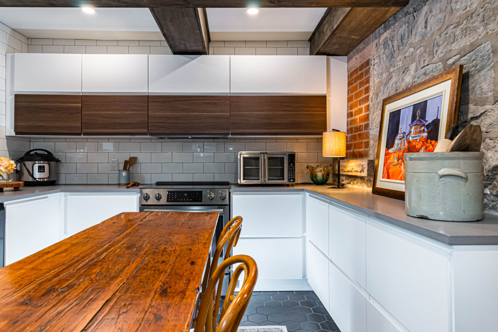 Example of a mid-sized mountain style u-shaped ceramic tile, black floor and exposed beam eat-in kitchen design in Toronto with a farmhouse sink, flat-panel cabinets, white cabinets, quartz countertops, white backsplash, subway tile backsplash, stainless steel appliances, an island and gray countertops