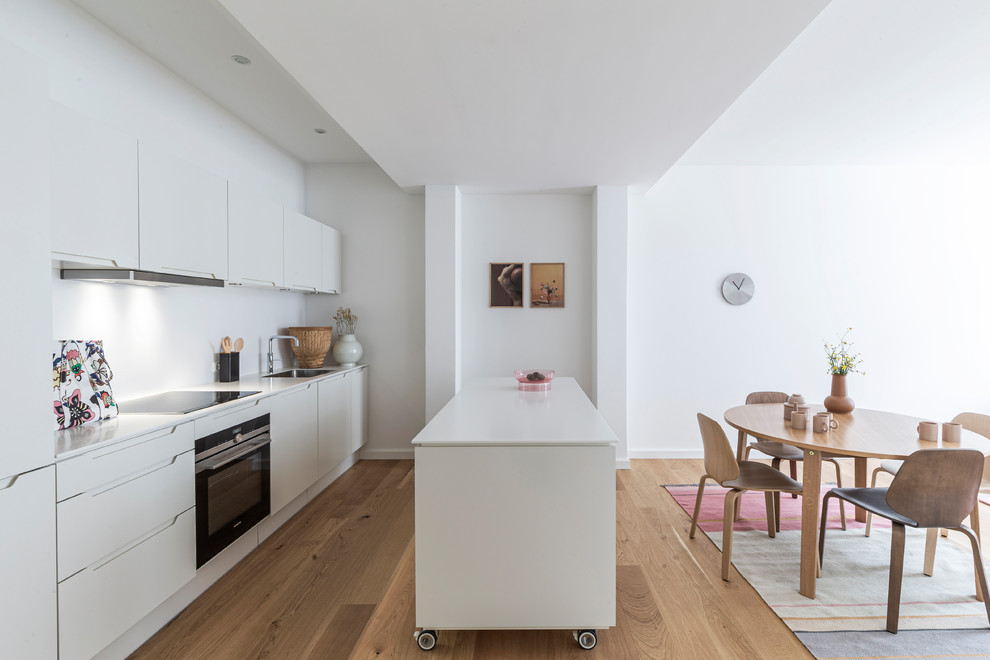 Design ideas for a scandinavian single-wall eat-in kitchen in Copenhagen with a single-bowl sink, flat-panel cabinets, white cabinets, white splashback, light hardwood floors, with island, beige floor and white benchtop.