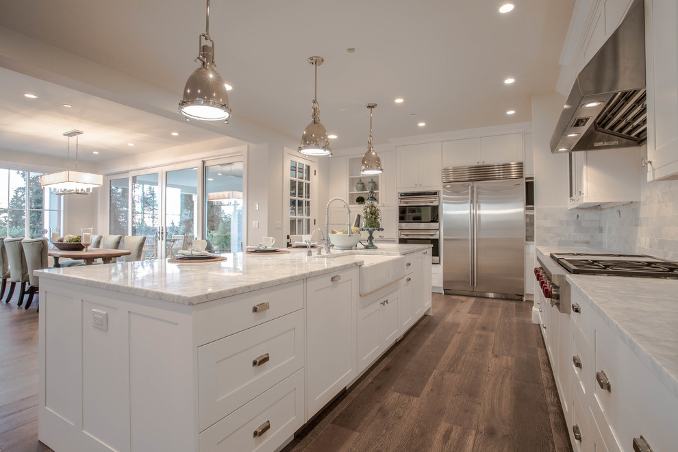 Design ideas for an expansive country l-shaped open plan kitchen in Seattle with a farmhouse sink, shaker cabinets, white cabinets, marble benchtops, white splashback, stone tile splashback, stainless steel appliances, dark hardwood floors and with island.