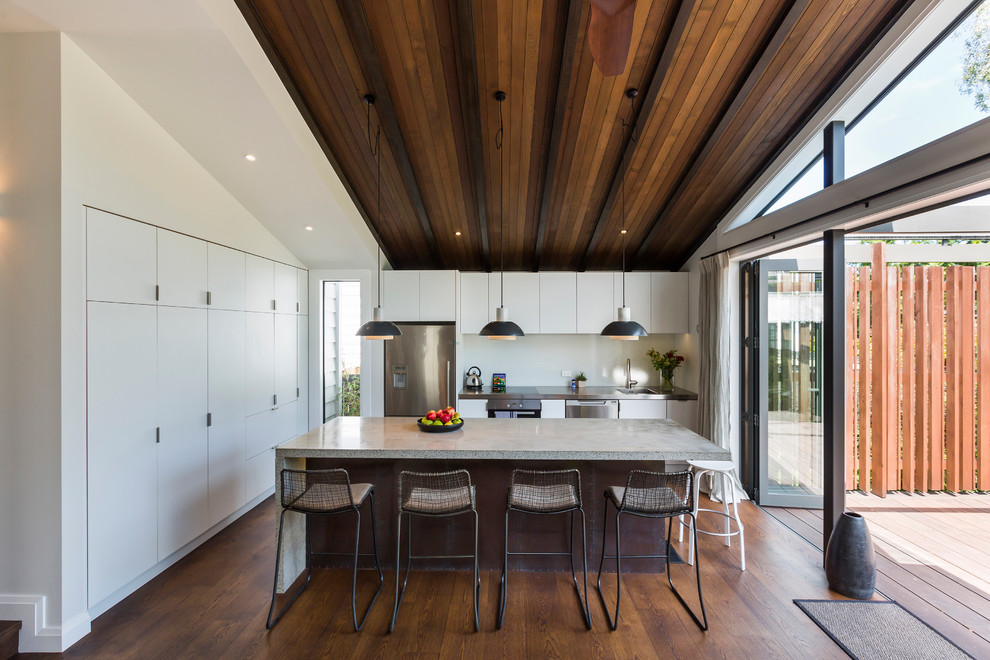 Contemporary kitchen in Auckland with white splashback, stainless steel appliances, with island, flat-panel cabinets, white cabinets and dark hardwood floors.
