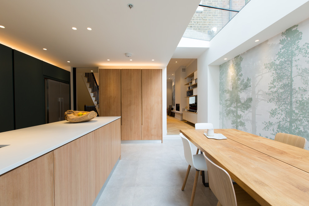 Inspiration for an expansive contemporary open plan kitchen in London with flat-panel cabinets, light wood cabinets, stainless steel appliances, concrete floors, with island, grey floor, a drop-in sink, solid surface benchtops, white splashback, marble splashback and white benchtop.