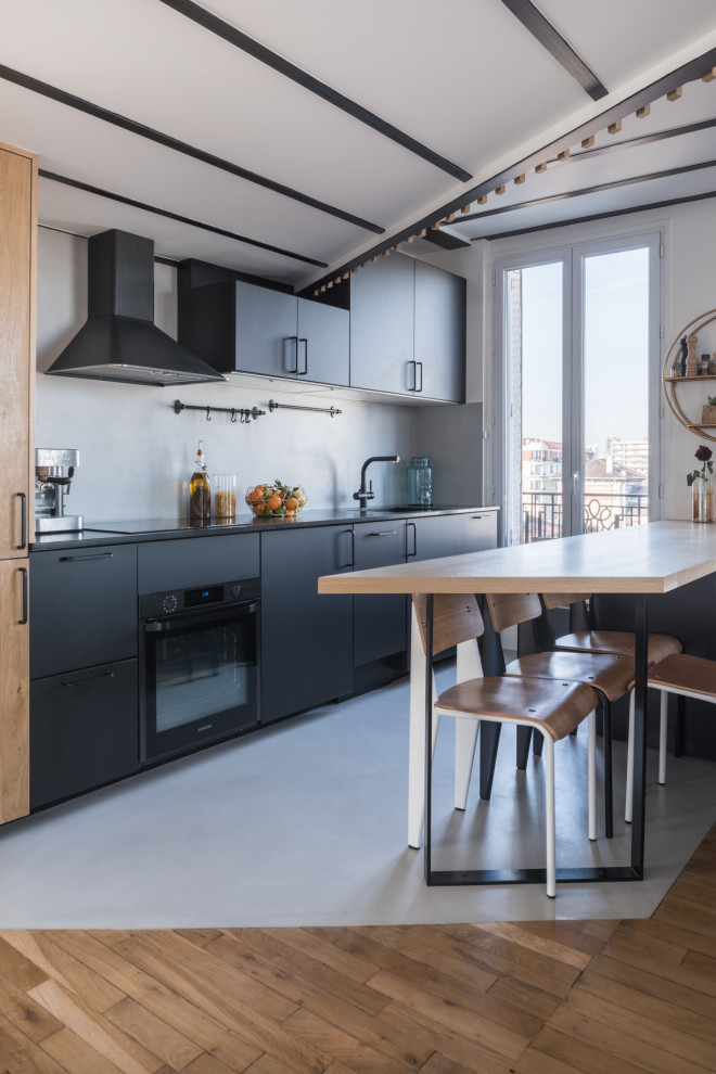 Inspiration for a mid-sized contemporary galley open plan kitchen in Paris with an integrated sink, flat-panel cabinets, black cabinets, grey splashback, black appliances, porcelain floors, a peninsula, grey floor and black benchtop.