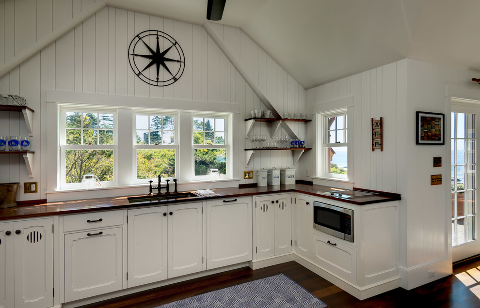 Design ideas for a beach style l-shaped kitchen in Portland Maine with recessed-panel cabinets, white cabinets, dark hardwood floors, no island, an undermount sink, wood benchtops, white splashback and black appliances.