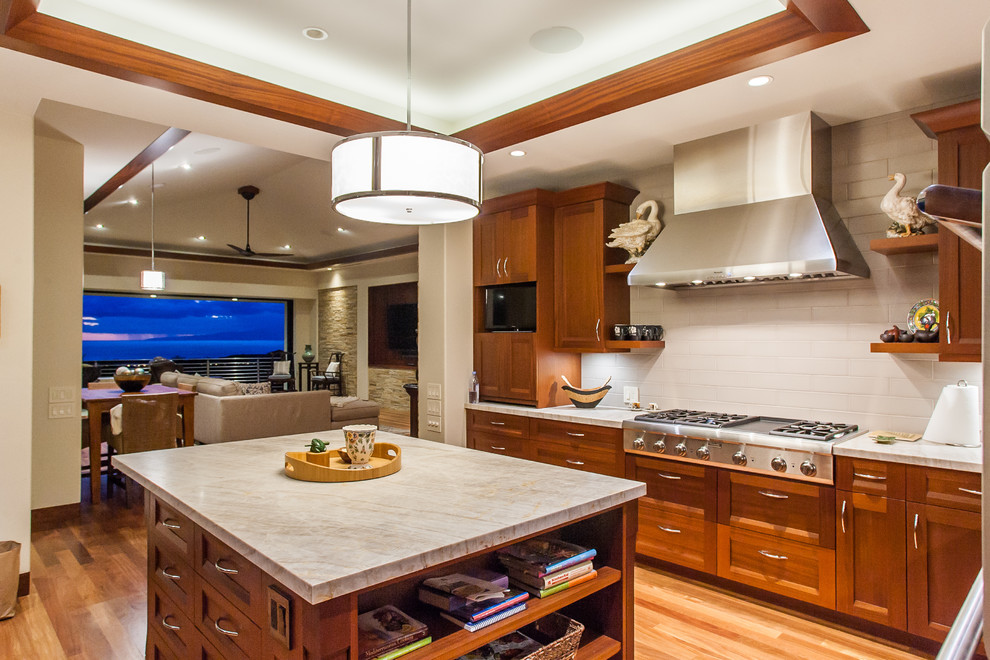 This is an example of a tropical open plan kitchen in Hawaii with shaker cabinets, medium wood cabinets, marble benchtops, stainless steel appliances, medium hardwood floors and with island.