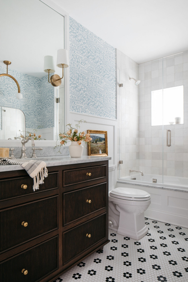 This is an example of a traditional bathroom in Chicago with flat-panel cabinets, dark wood cabinets, an alcove tub, a shower/bathtub combo, white tile, blue walls, mosaic tile floors, an undermount sink, multi-coloured floor, a hinged shower door, grey benchtops, a single vanity, a freestanding vanity, decorative wall panelling and wallpaper.