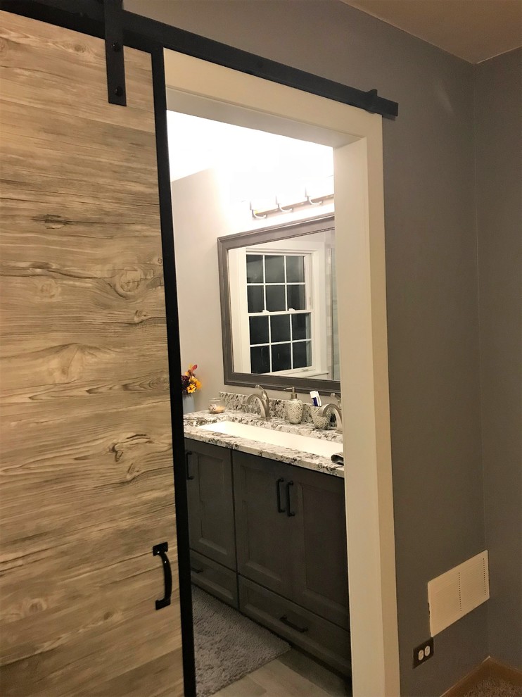 Design ideas for a mid-sized country master bathroom in Milwaukee with flat-panel cabinets, grey cabinets, an alcove shower, gray tile, porcelain tile, beige walls, porcelain floors, a trough sink, granite benchtops, grey floor, a hinged shower door and grey benchtops.