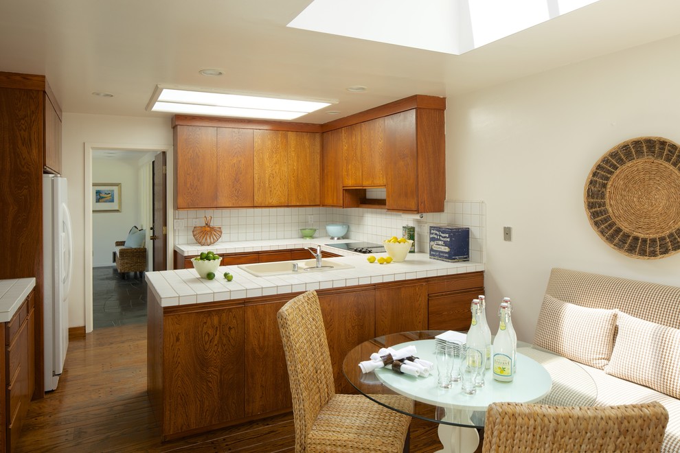 This is an example of a midcentury eat-in kitchen in San Francisco with a drop-in sink, flat-panel cabinets, medium wood cabinets, tile benchtops, white splashback and white appliances.