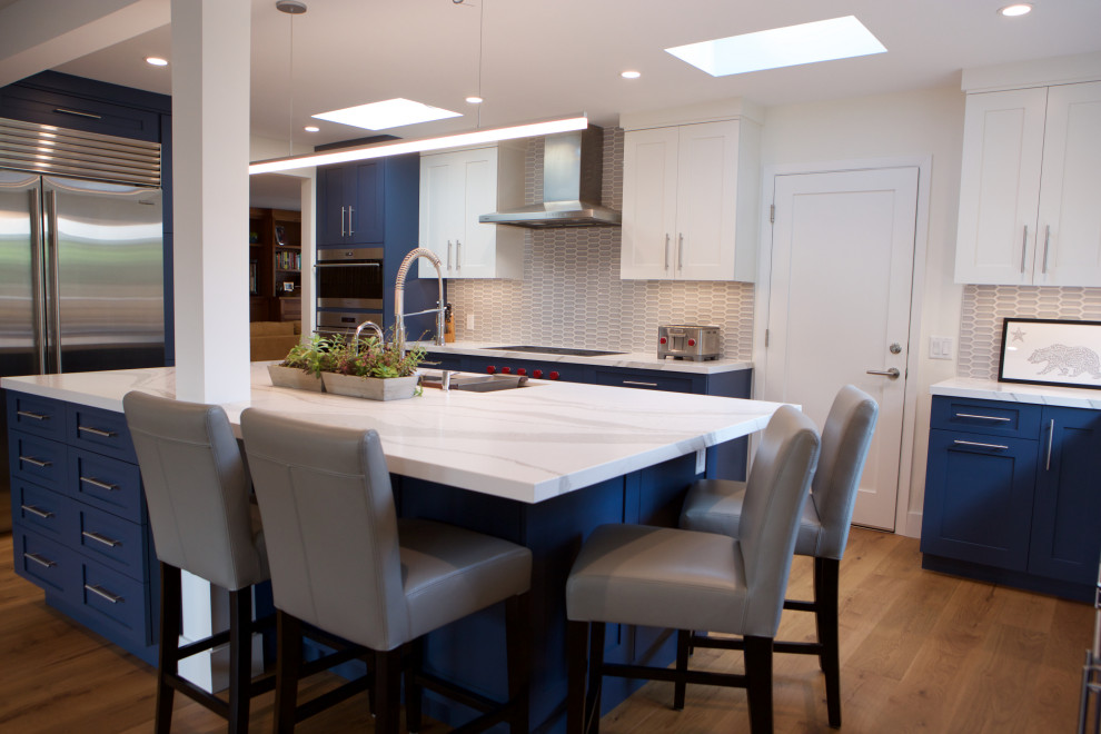 Inspiration for a large transitional u-shaped medium tone wood floor open concept kitchen remodel in San Francisco with a single-bowl sink, recessed-panel cabinets, blue cabinets, quartz countertops, gray backsplash, mosaic tile backsplash, stainless steel appliances, an island and white countertops