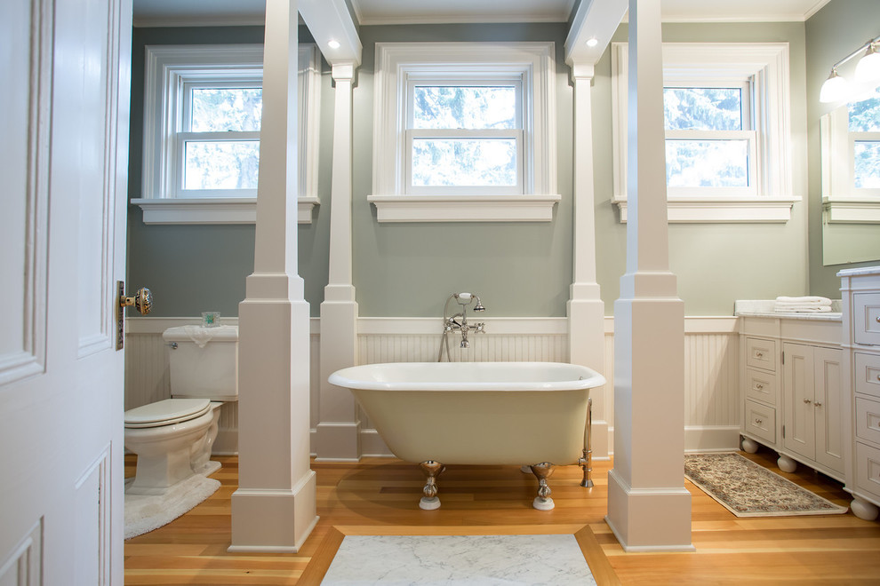 This is an example of a large traditional master bathroom in Seattle with beaded inset cabinets, white cabinets, a claw-foot tub, green walls, medium hardwood floors, a two-piece toilet, an undermount sink, marble benchtops and brown floor.