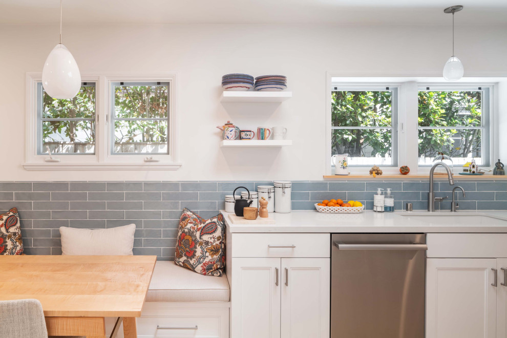 Photo of a medium sized classic galley kitchen/diner in Los Angeles with a submerged sink, shaker cabinets, white cabinets, engineered stone countertops, blue splashback, metro tiled splashback, stainless steel appliances, light hardwood flooring, a breakfast bar, beige floors and white worktops.