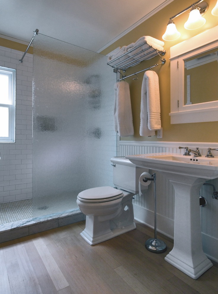 Mid-sized arts and crafts 3/4 bathroom in Seattle with white cabinets, an open shower, white tile, ceramic tile, beige walls, a pedestal sink, a two-piece toilet, light hardwood floors, beige floor and an open shower.