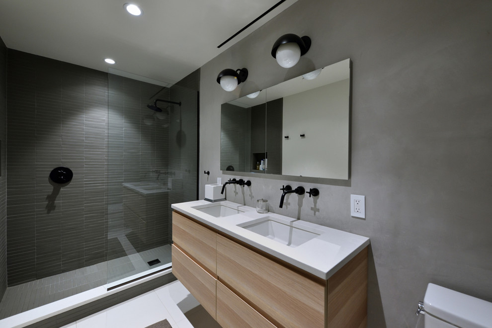 Design ideas for a mid-sized modern 3/4 bathroom in New York with flat-panel cabinets, light wood cabinets, an alcove shower, a two-piece toilet, gray tile, porcelain tile, grey walls, porcelain floors, an undermount sink, solid surface benchtops, white floor and an open shower.