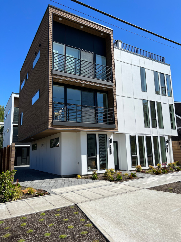 Photo of a large modern three-storey white duplex exterior in Seattle with concrete fiberboard siding, a flat roof, a metal roof, a black roof and board and batten siding.