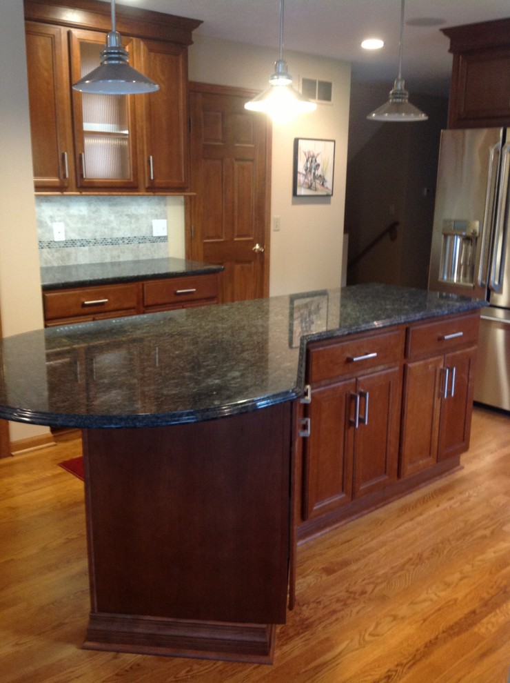Mid-sized transitional l-shaped medium tone wood floor eat-in kitchen photo with an undermount sink, recessed-panel cabinets, medium tone wood cabinets, granite countertops, gray backsplash, stone tile backsplash, stainless steel appliances, gray walls and an island