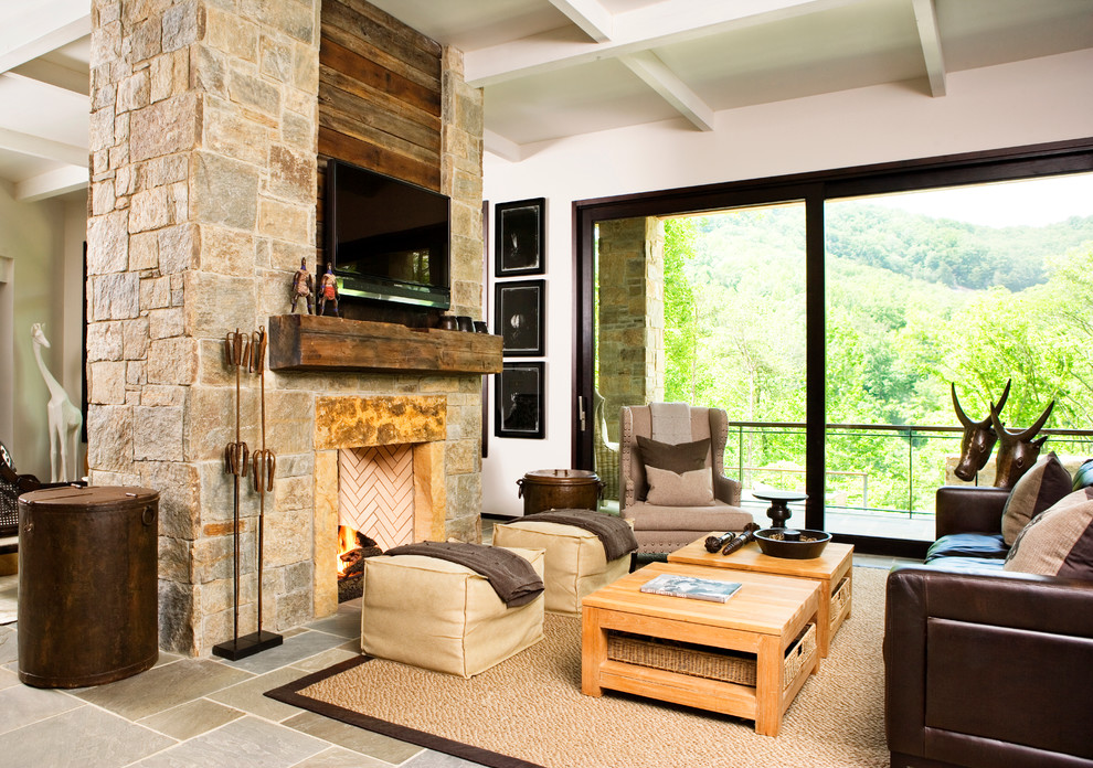 This is an example of a country open concept living room in Other with white walls, slate floors, a two-sided fireplace, a stone fireplace surround and a wall-mounted tv.