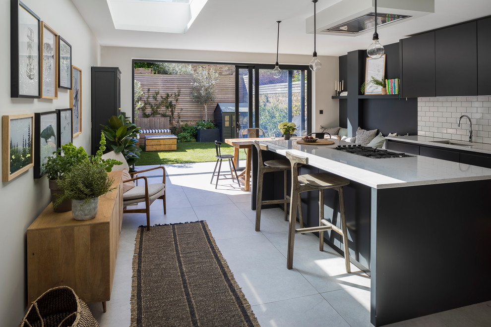 This is an example of a mid-sized contemporary single-wall eat-in kitchen in London with ceramic floors, grey floor, an undermount sink, flat-panel cabinets, black cabinets, white splashback, subway tile splashback, black appliances, with island and white benchtop.