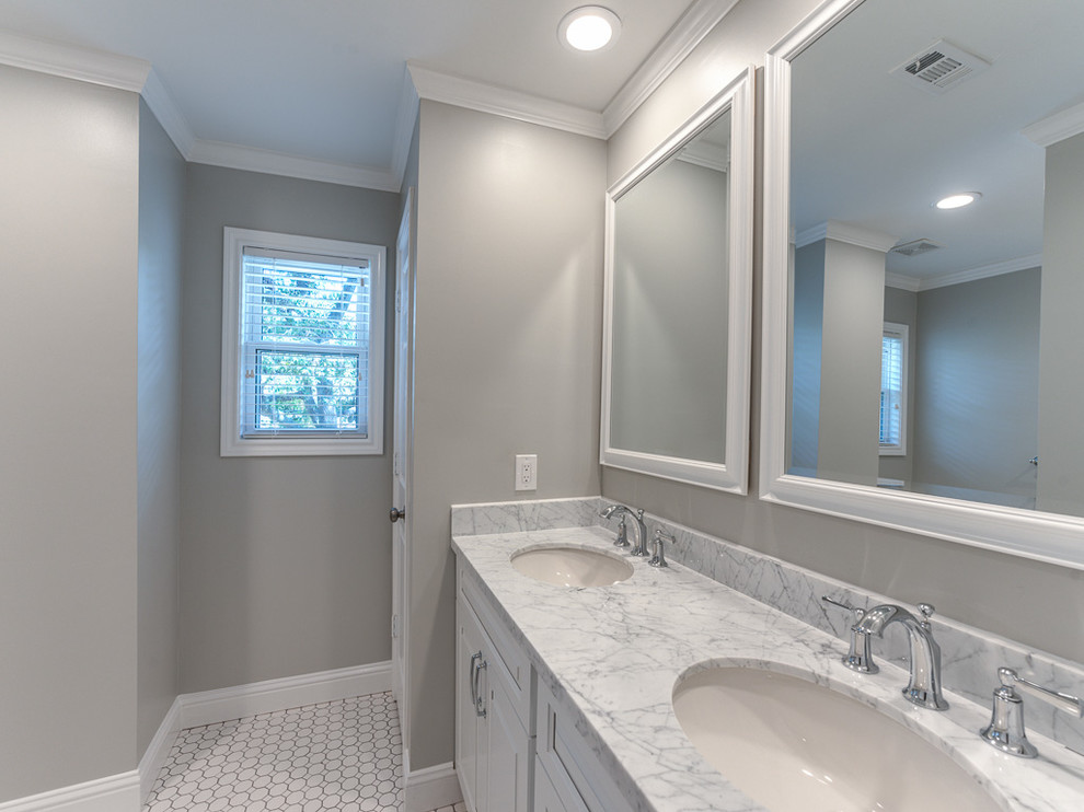 This is an example of a mid-sized traditional kids bathroom in Houston with raised-panel cabinets, white cabinets, an alcove tub, a double shower, a one-piece toilet, white tile, subway tile, grey walls, porcelain floors, an undermount sink and marble benchtops.