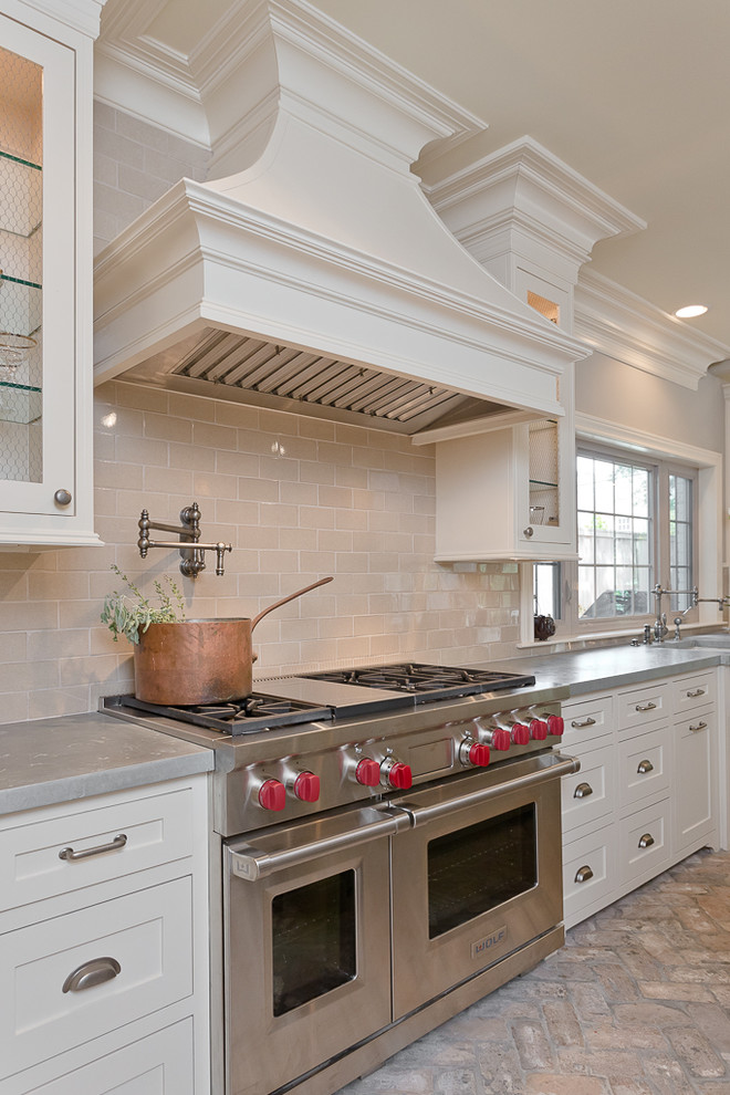 Mid-sized traditional u-shaped open plan kitchen in Houston with a farmhouse sink, recessed-panel cabinets, white cabinets, zinc benchtops, beige splashback, stainless steel appliances, brick floors and with island.
