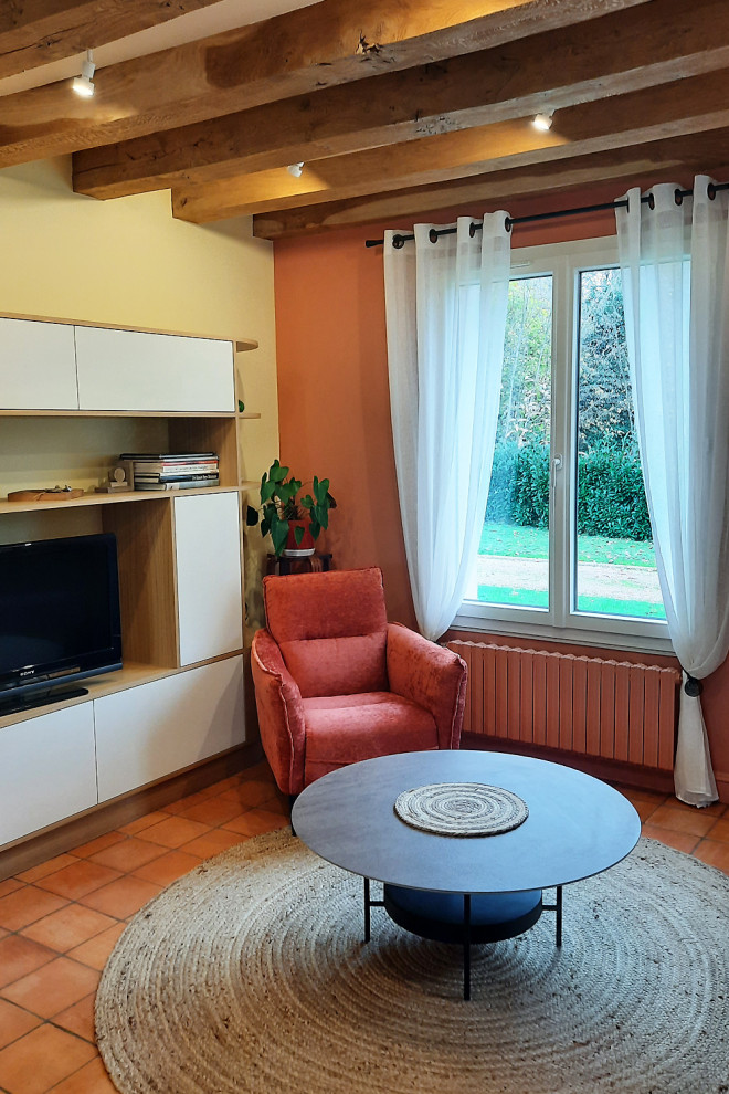 Landhausstil Wohnzimmer mit oranger Wandfarbe, Terrakottaboden, freistehendem TV, orangem Boden und freigelegten Dachbalken in Angers