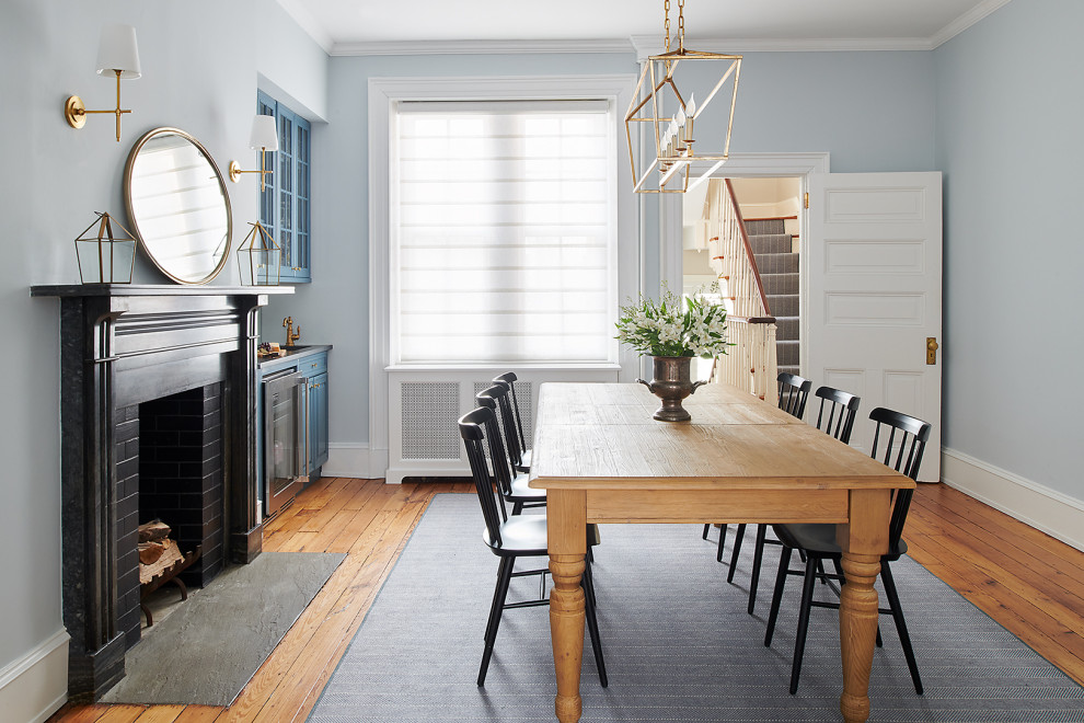 Photo of a small transitional dining room in Philadelphia with blue walls, light hardwood floors, a corner fireplace, a stone fireplace surround and brown floor.