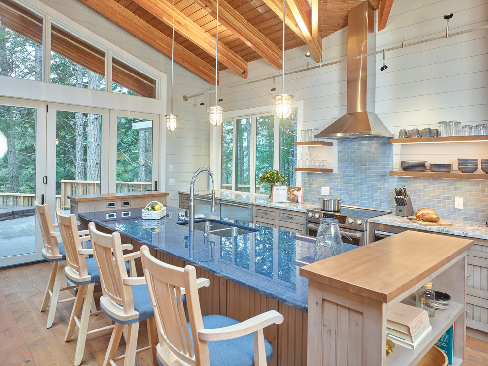 Mid-sized mountain style galley medium tone wood floor and brown floor open concept kitchen photo with an undermount sink, beaded inset cabinets, medium tone wood cabinets, glass countertops, blue backsplash, ceramic backsplash, stainless steel appliances, an island and blue countertops