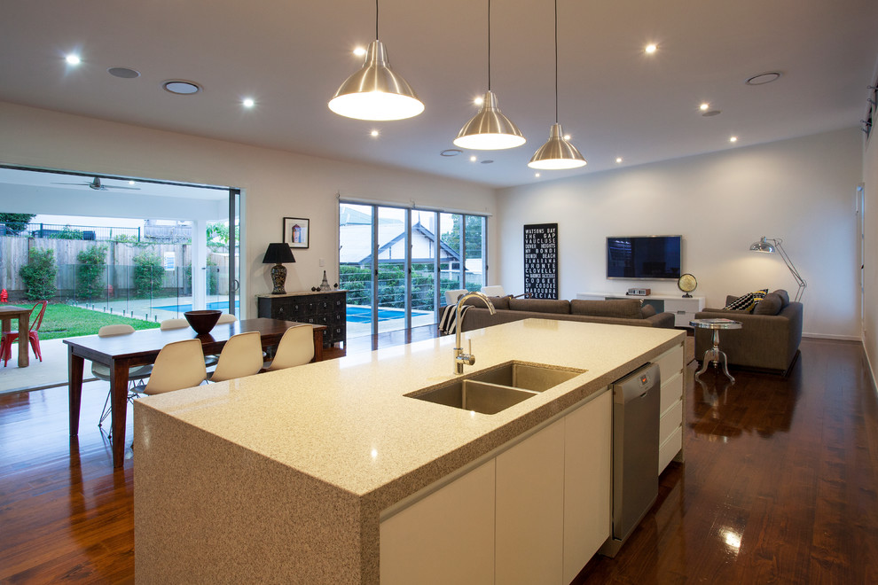 Inspiration for a large contemporary l-shaped open plan kitchen in Brisbane with a double-bowl sink, white cabinets, solid surface benchtops, metallic splashback, glass sheet splashback, stainless steel appliances, medium hardwood floors and with island.