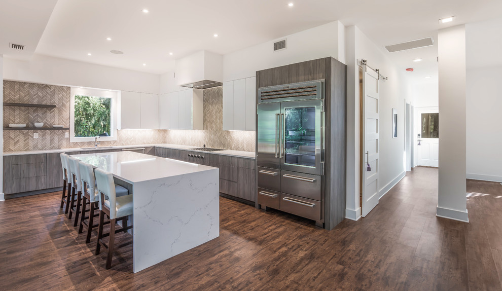 Large contemporary l-shaped open plan kitchen in Jacksonville with an undermount sink, flat-panel cabinets, quartz benchtops, stainless steel appliances, with island, brown floor, white benchtop, medium wood cabinets, mosaic tile splashback, beige splashback and vinyl floors.