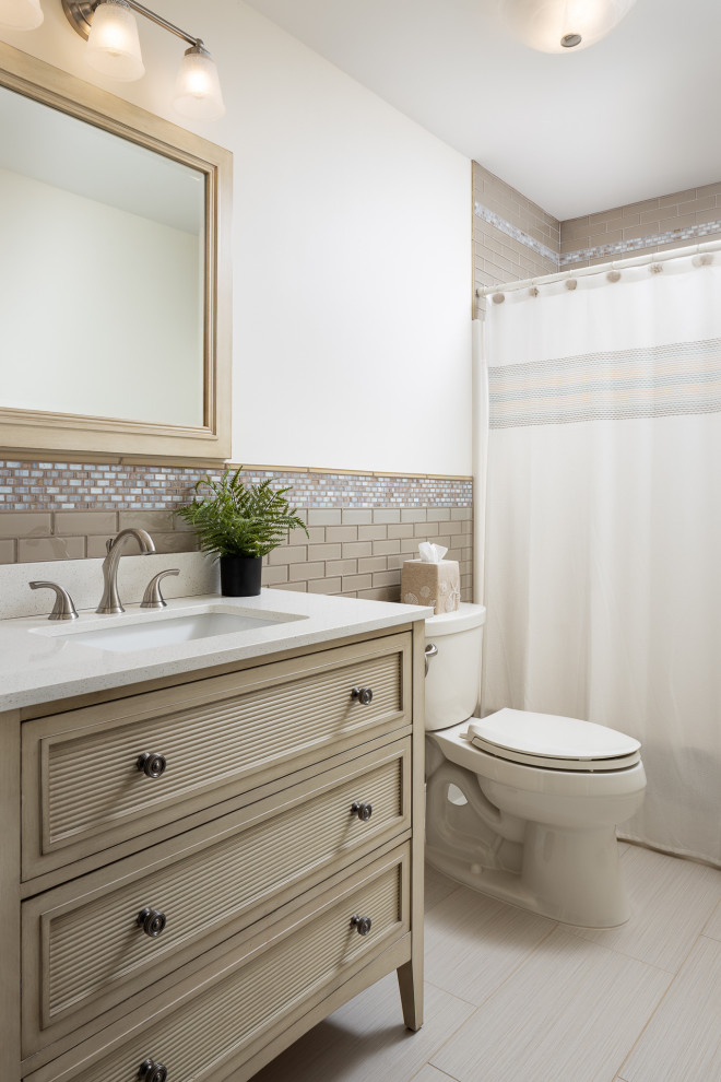 This is an example of a mid-sized beach style bathroom in New York with beige cabinets, an alcove tub, a shower/bathtub combo, a two-piece toilet, beige tile, subway tile, white walls, porcelain floors, an undermount sink, marble benchtops, multi-coloured floor, a shower curtain, white benchtops, a single vanity and a freestanding vanity.