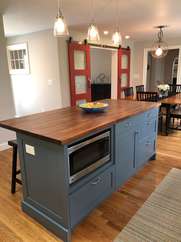 Open concept kitchen - mid-sized transitional l-shaped medium tone wood floor and brown floor open concept kitchen idea in Boston with a single-bowl sink, shaker cabinets, white cabinets, granite countertops, white backsplash, window backsplash, stainless steel appliances, an island and black countertops