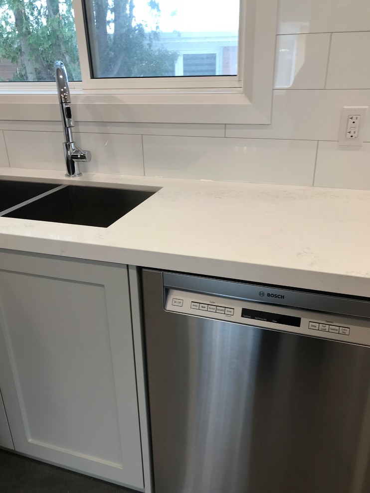 Example of a mid-sized transitional porcelain tile and brown floor home design design in Toronto with an undermount sink, shaker cabinets, gray cabinets, quartz countertops, white backsplash, subway tile backsplash, stainless steel appliances, an island and white countertops