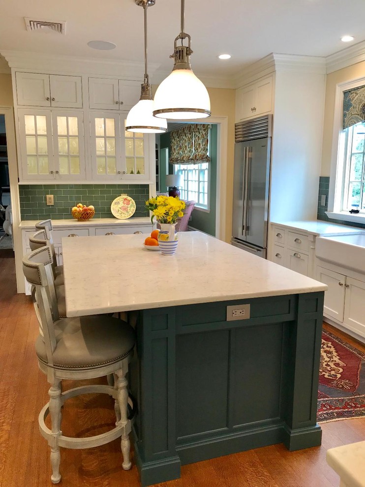 Photo of a large traditional l-shaped eat-in kitchen in New York with a farmhouse sink, beaded inset cabinets, white cabinets, quartz benchtops, green splashback, subway tile splashback, stainless steel appliances, light hardwood floors, with island, brown floor and white benchtop.