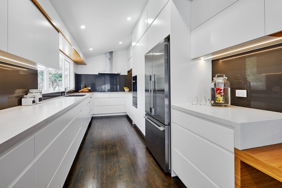 This is an example of a large contemporary galley eat-in kitchen in Sydney with a double-bowl sink, flat-panel cabinets, white cabinets, quartz benchtops, grey splashback, stone slab splashback, stainless steel appliances, painted wood floors, no island and grey floor.