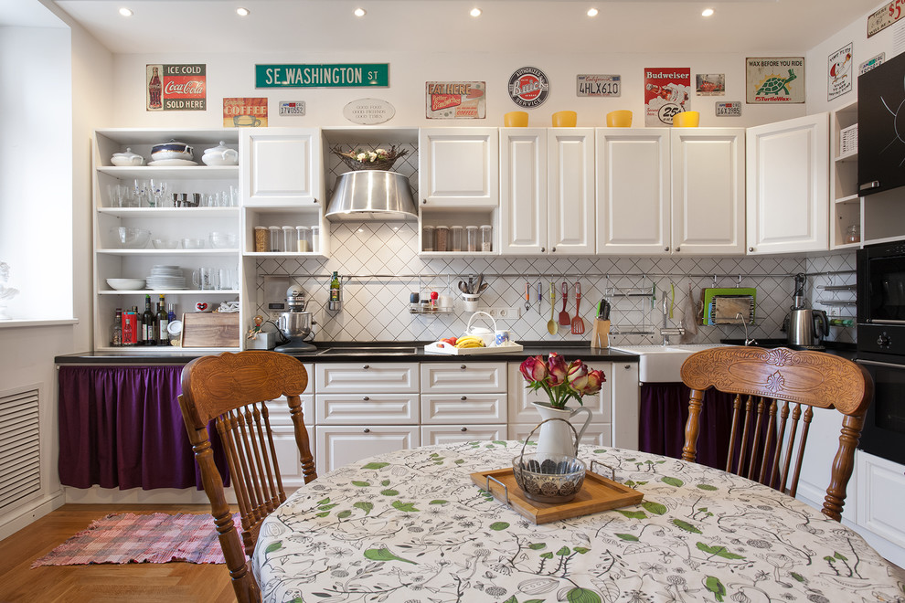 This is an example of an eclectic l-shaped kitchen in Moscow with raised-panel cabinets, white cabinets, white splashback, black appliances, no island, a farmhouse sink and medium hardwood floors.
