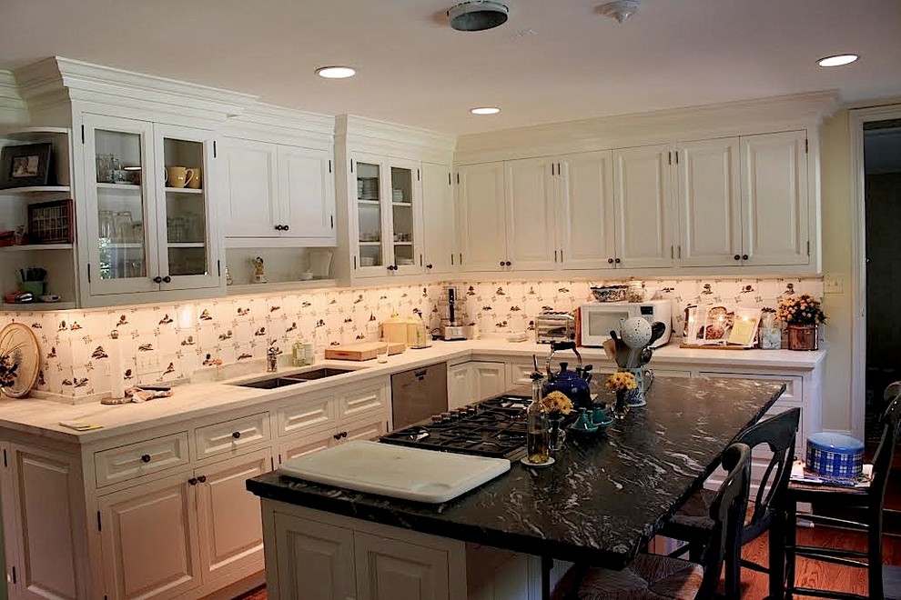 Example of a mid-sized transitional l-shaped medium tone wood floor enclosed kitchen design in Chicago with a double-bowl sink, raised-panel cabinets, white cabinets, quartz countertops, white backsplash, ceramic backsplash, stainless steel appliances and an island