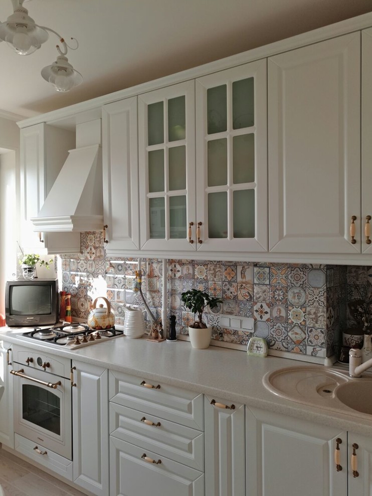 This is an example of a small country single-wall eat-in kitchen in Other with a drop-in sink, raised-panel cabinets, white cabinets, laminate benchtops, multi-coloured splashback, white appliances and beige benchtop.
