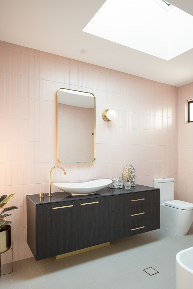 Идея дизайна: ванная комната среднего размера в современном стиле с темными деревянными фасадами, отдельно стоящей ванной, открытым душем, унитазом-моноблоком, розовой плиткой, удлиненной плиткой, розовыми стенами, полом из керамической плитки, душевой кабиной, настольной раковиной, столешницей из ламината, серым полом, открытым душем, черной столешницей, тумбой под одну раковину, подвесной тумбой и плоскими фасадами