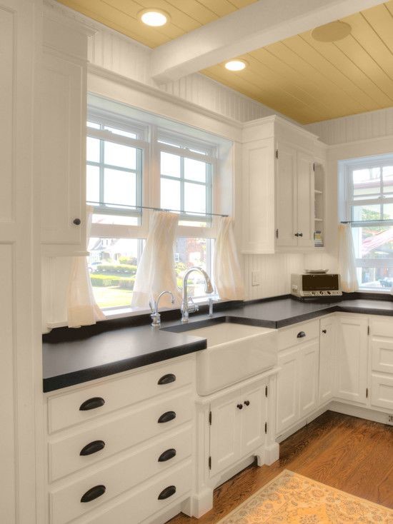 Design ideas for a mid-sized country l-shaped separate kitchen in Portland with a farmhouse sink, recessed-panel cabinets, white cabinets, solid surface benchtops, white splashback, timber splashback, medium hardwood floors, no island, brown floor and black benchtop.
