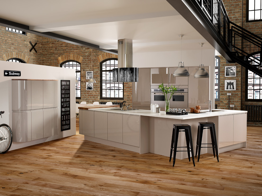 This is an example of an expansive industrial u-shaped open plan kitchen in Wiltshire with flat-panel cabinets, white cabinets, stainless steel appliances, light hardwood floors and a peninsula.